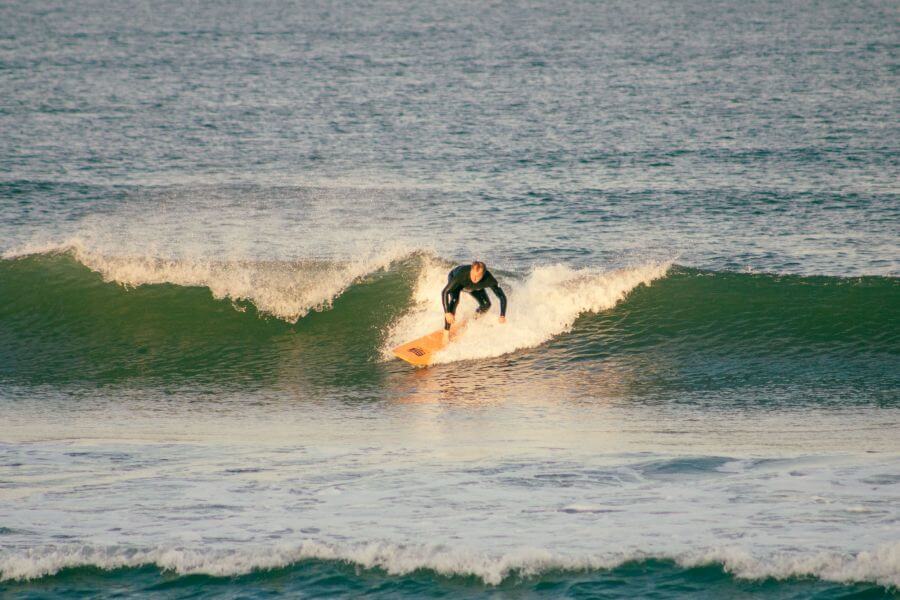 Goodtimes Surfkurs Teilnehmer Rafael surft eine schöne grüne Welle im Sonnenaufgang